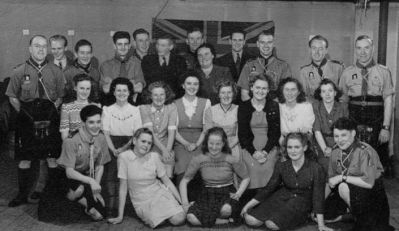 Undated black-and-white group photo of uniformed Scout leaders and young women posing in three rows in a hall