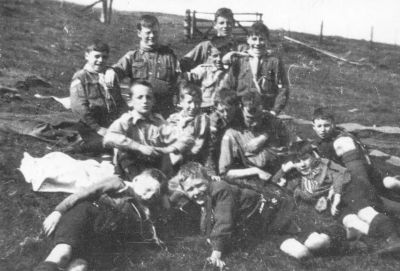 Black-and-white photo of a group of about 15 boy Scouts in uniform sitting and lying on a grassy hillside